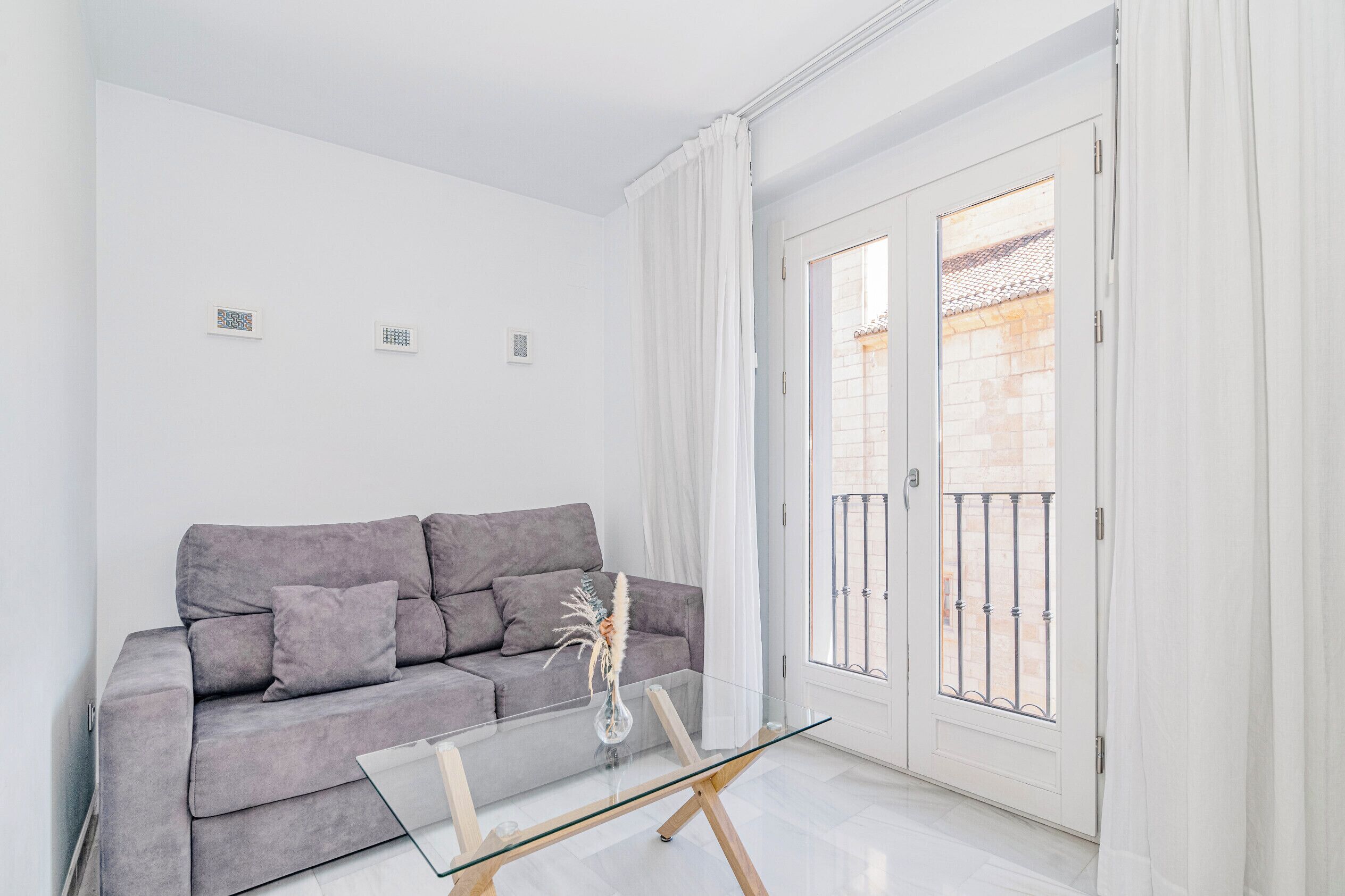 A modern living room with a grey sofa, a glass coffee table, and a door leading to a balcony.