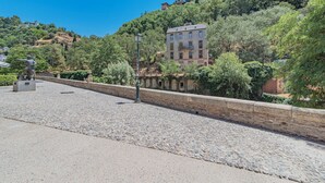 Un'area pavimentata con una statua, un muro in pietra e un edificio con una torre su una collina.