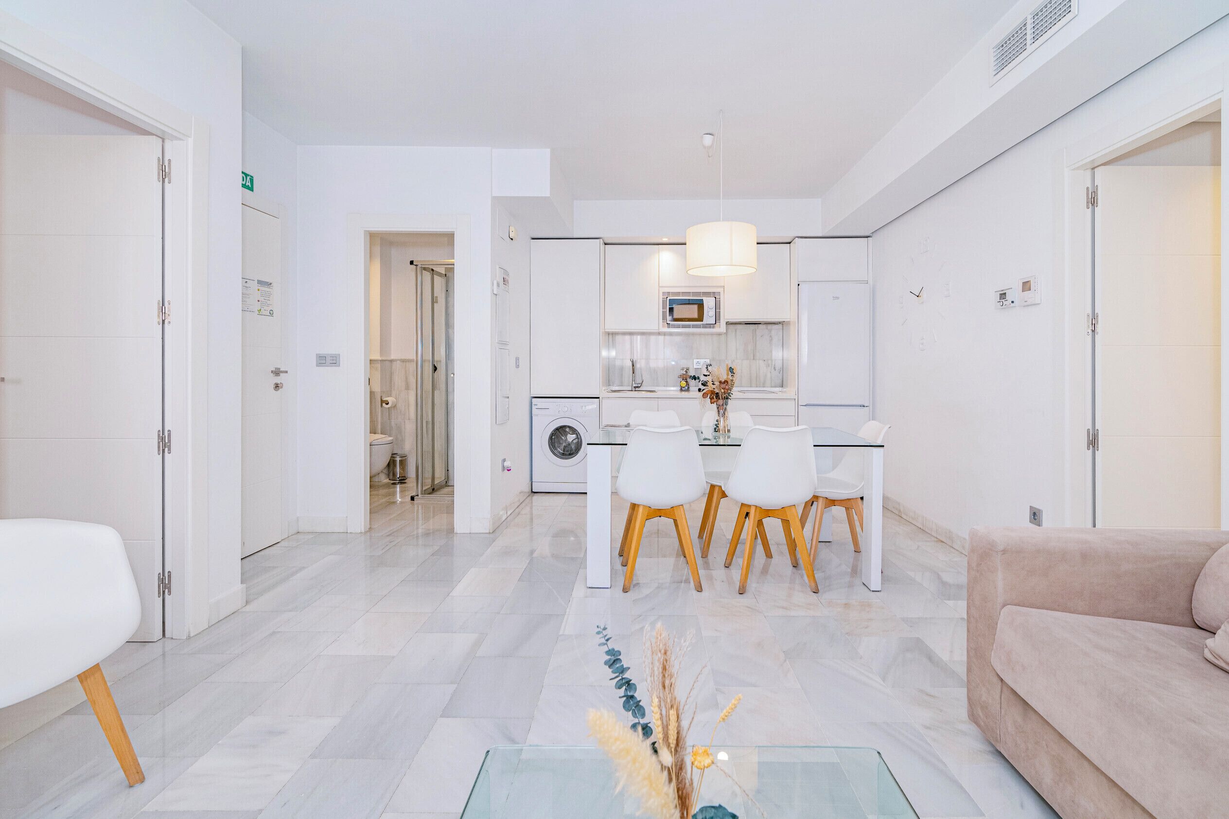 A modern kitchen with white cabinets, a dining area with a table and chairs, and a living area with a sofa.