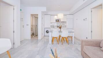 A modern kitchen with white cabinets, a dining area with a table and chairs, and a living area with a sofa.