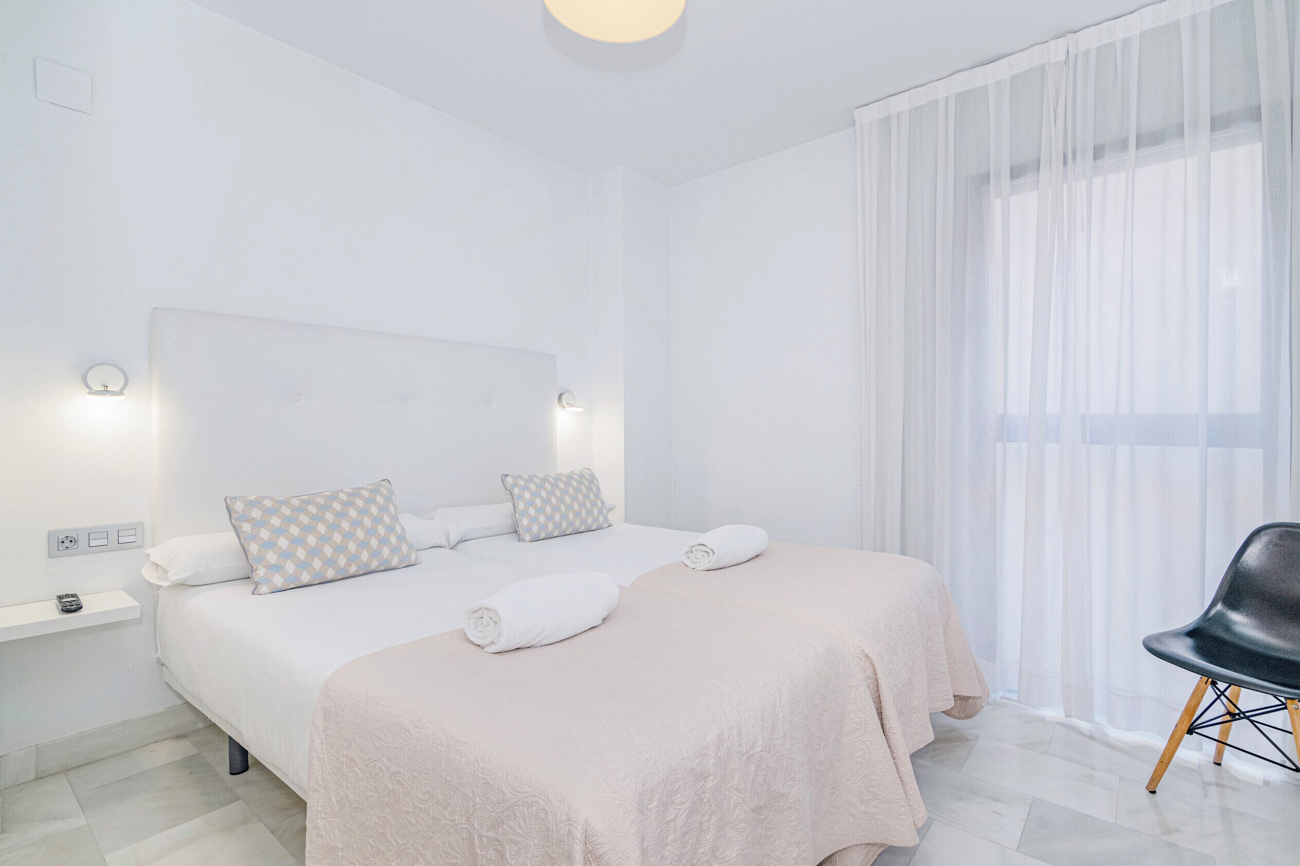 Une chambre d’hôtel avec un grand lit, une table de chevet avec une télécommande et des rideaux légers.