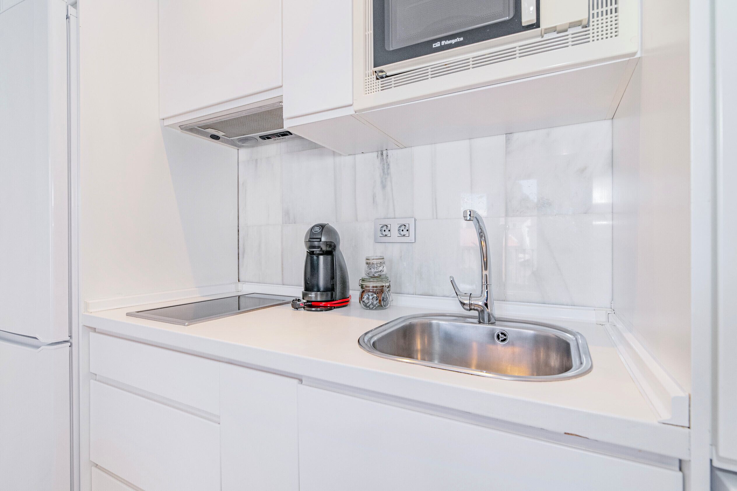 Een moderne keuken met witte kasten, een roestvrijstalen spoelbak, een koffiezetapparaat en een magnetron boven het aanrecht.