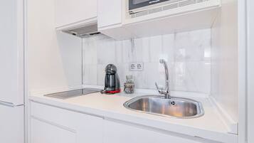 Een moderne keuken met witte kasten, een roestvrijstalen spoelbak, een koffiezetapparaat en een magnetron boven het aanrecht.