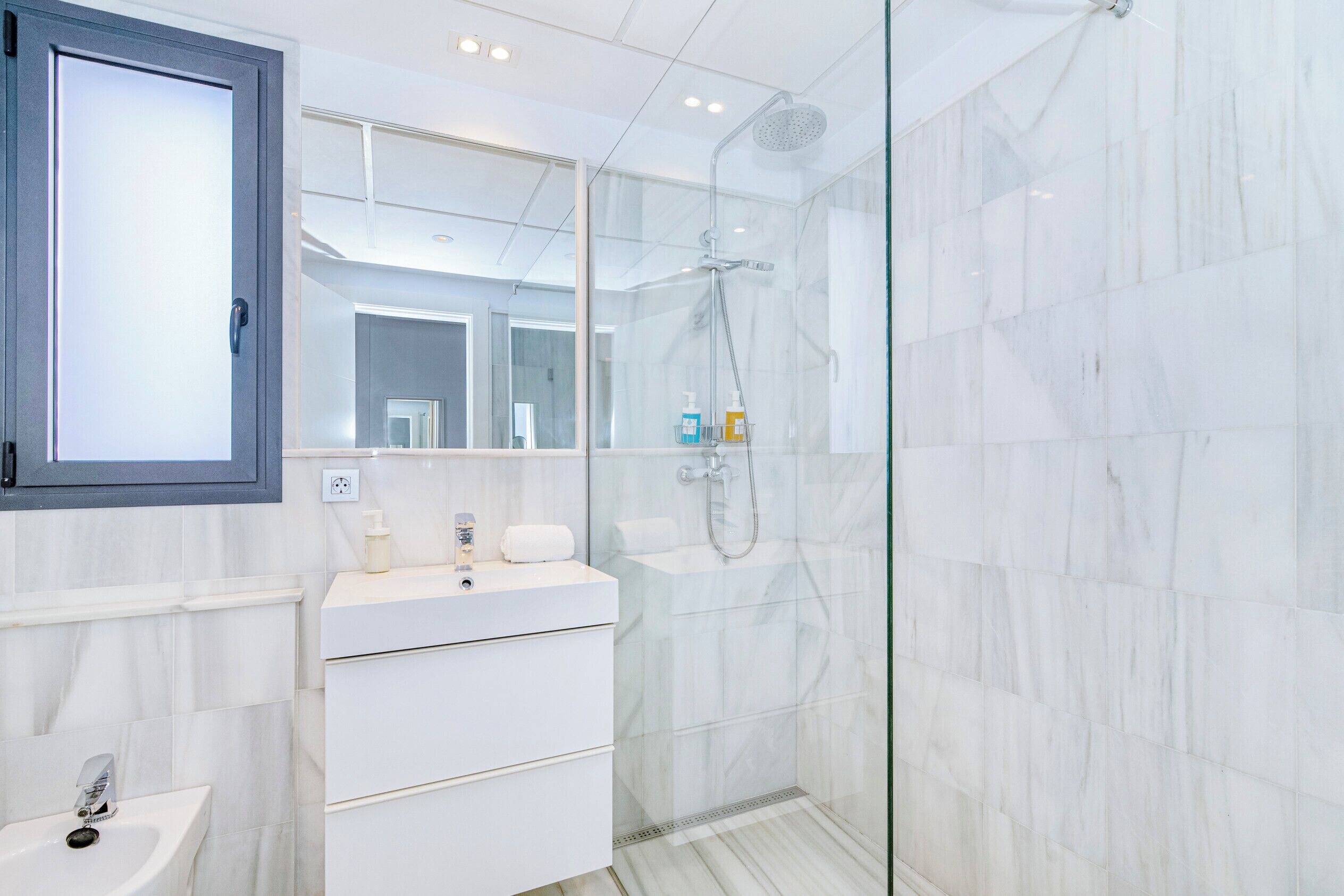 Une salle de bain moderne avec une douche à parois de verre, un meuble-lavabo blanc avec un miroir et un évier.