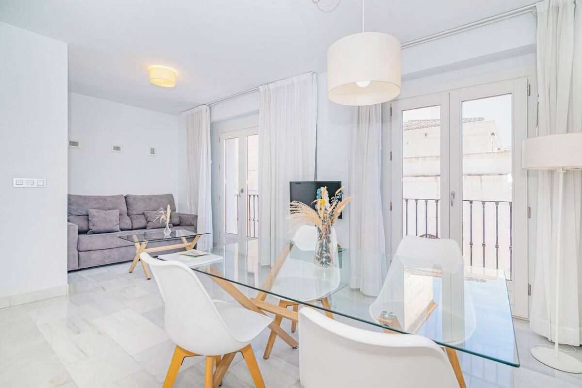 Una sala de estar moderna con una mesa de comedor de vidrio, sillas blancas, un sofá gris y un televisor.