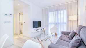 Un soggiorno moderno con un tavolino in vetro, un divano grigio, una TV a schermo piatto e una poltrona bianca.