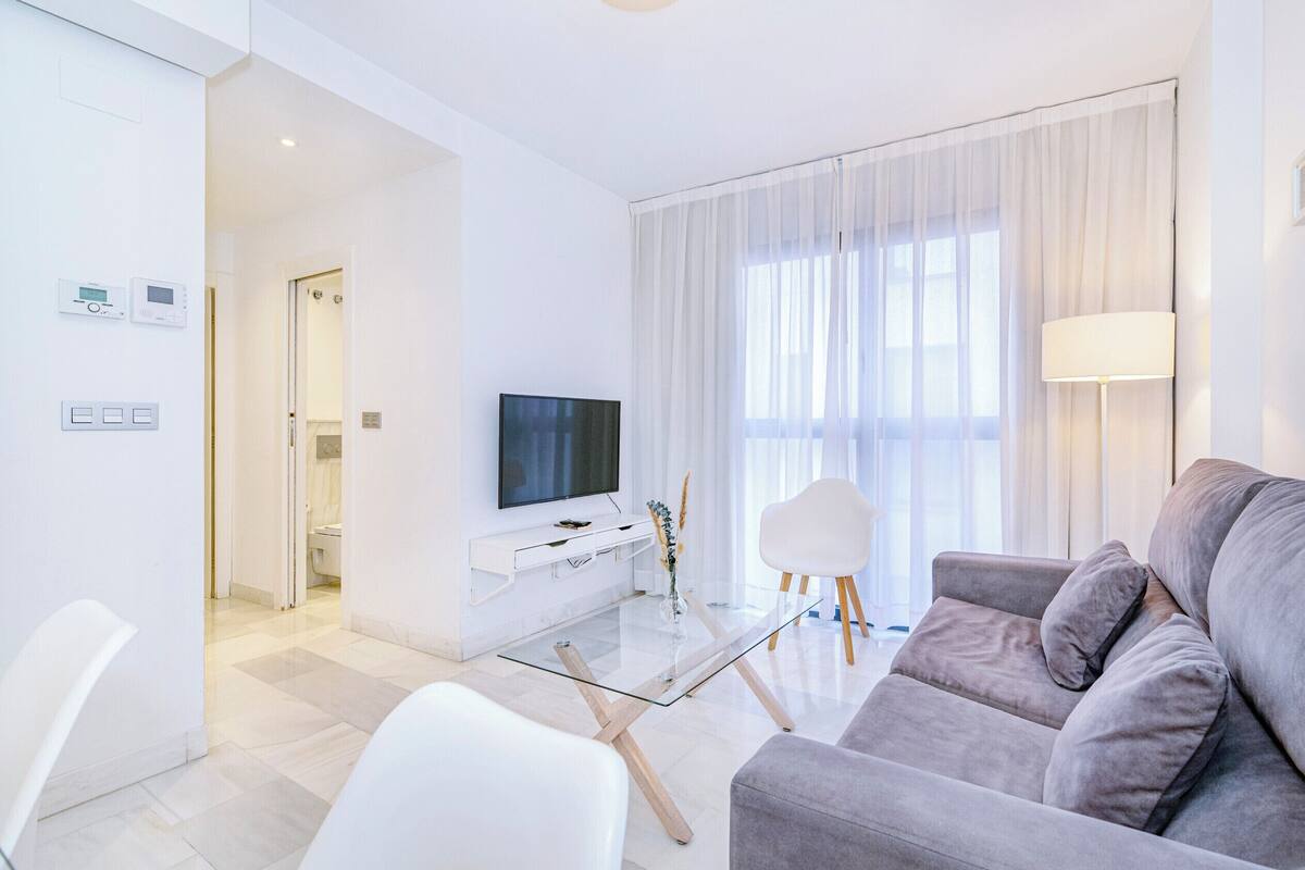 Una sala de estar moderna con una mesa de centro de vidrio, un sofá gris, un televisor de pantalla plana y una silla blanca.