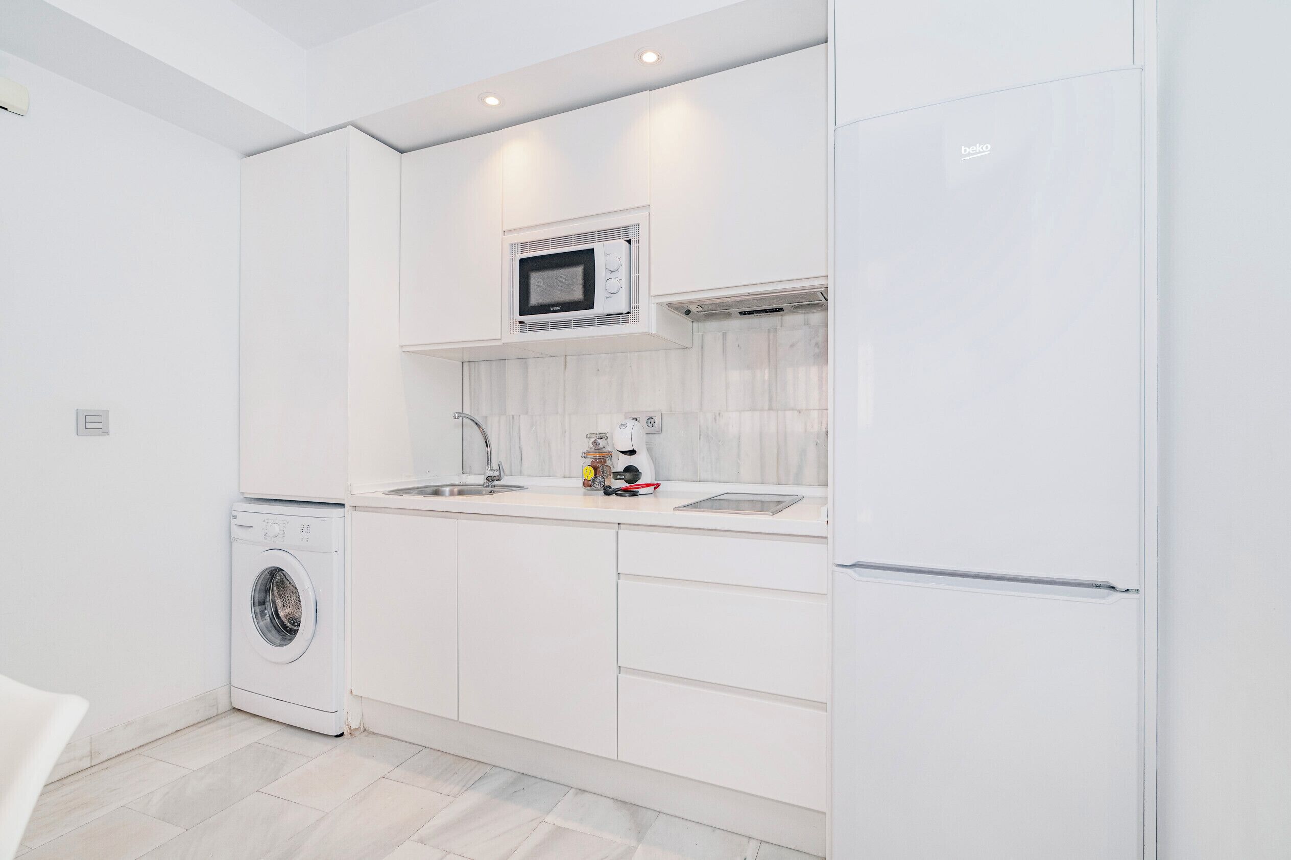 Une cuisine moderne avec des meubles blancs, un four à micro-ondes encastré, un lave-linge et un réfrigérateur.