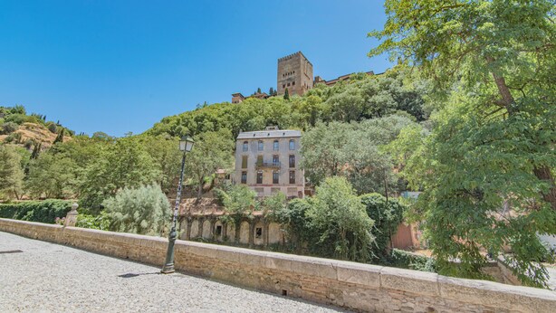 Un edificio storico con una torre, immerso nel verde e circondato da un muro in pietra.