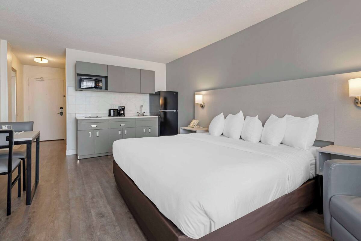 A modern hotel room with a large bed, a kitchenette, a dining area, and a bathroom.