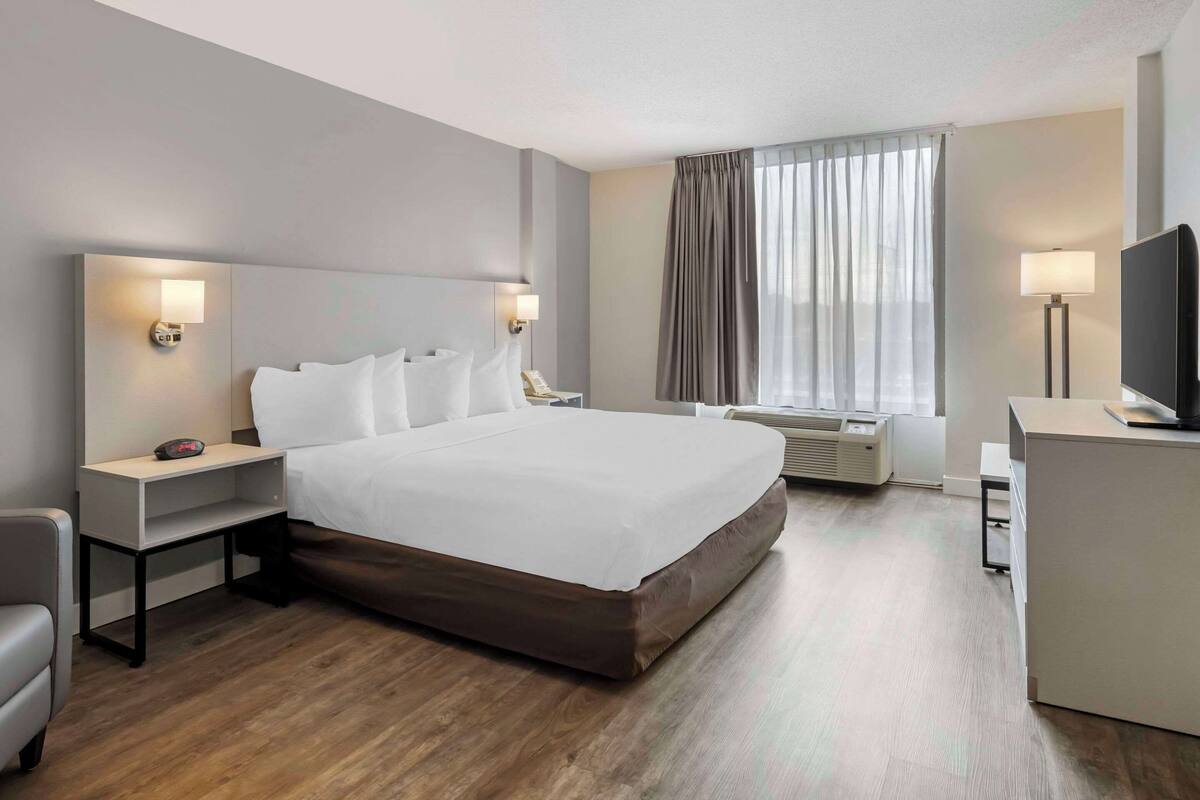 A hotel room with a large bed, bedside tables with lamps, a desk with a TV, and a window with curtains.