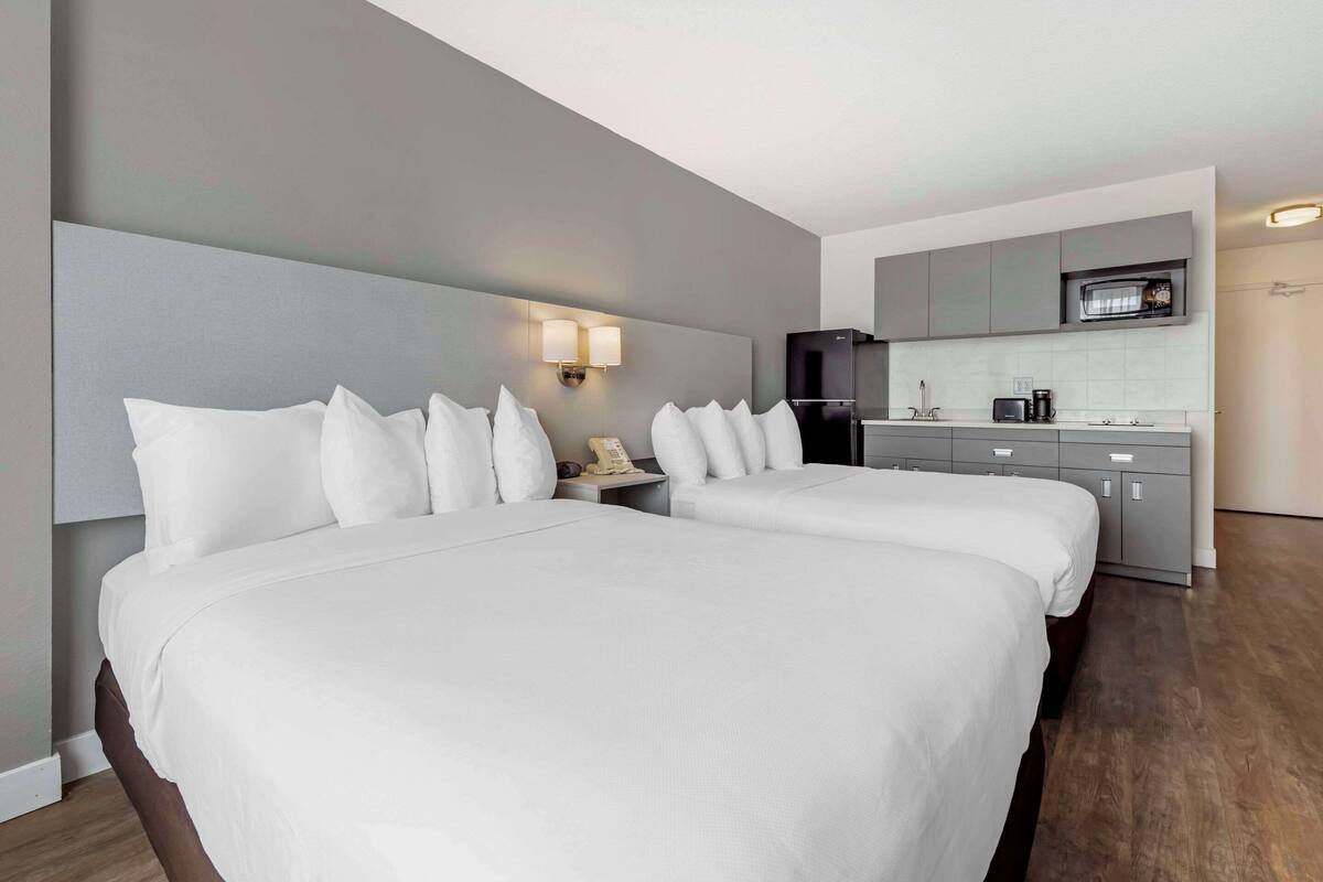A hotel room with two beds, a small kitchenette, and a microwave.