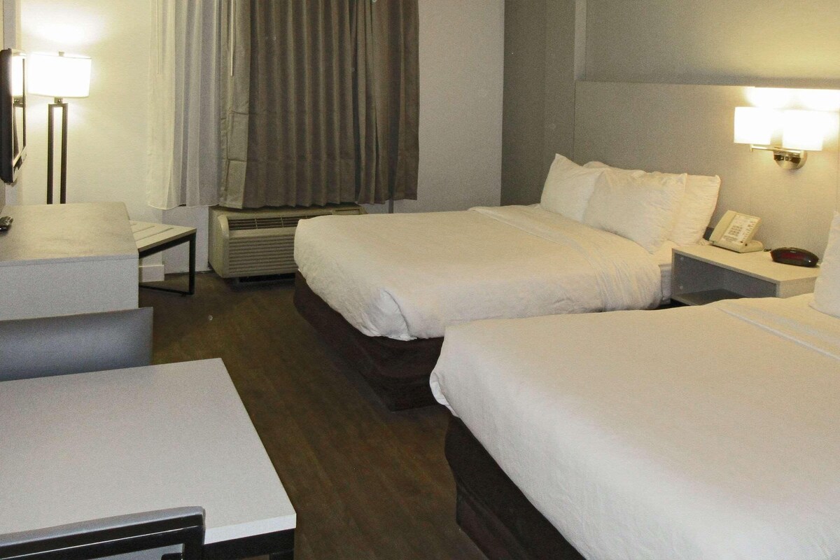 A hotel room with two beds, a desk, a chair, a lamp, and a telephone.