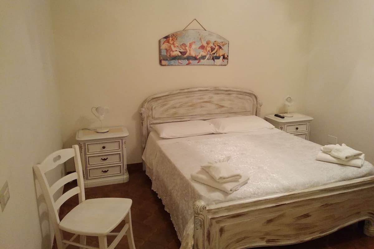 Une chambre à coucher avec un lit, une table de chevet, une chaise et un tableau accroché au mur.
