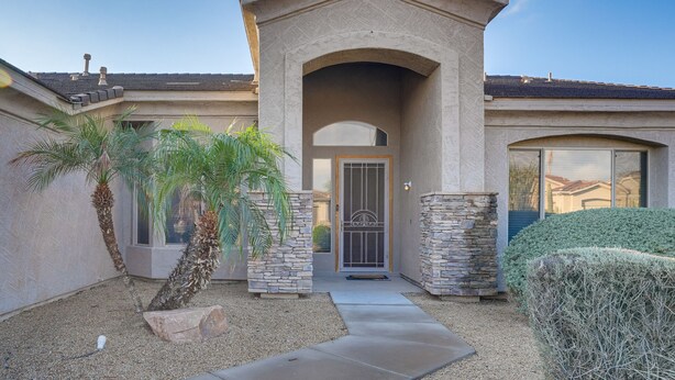 A residential building with a stone facade, a central entrance with a decorative arch, and a small garden with palm trees. - Goodyear Group Getaway w/ Pool & Putting Green (Goodyear)