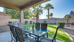 An outdoor patio with a glass table and metal chairs, surrounded by a well-maintained lawn and palm trees. - Goodyear Group Getaway w/ Pool & Putting Green (Goodyear)
