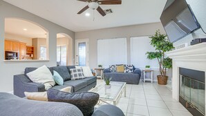 A spacious living room with a fireplace, a ceiling fan, and a kitchen area visible through an archway. - Goodyear Group Getaway w/ Pool & Putting Green (Goodyear)