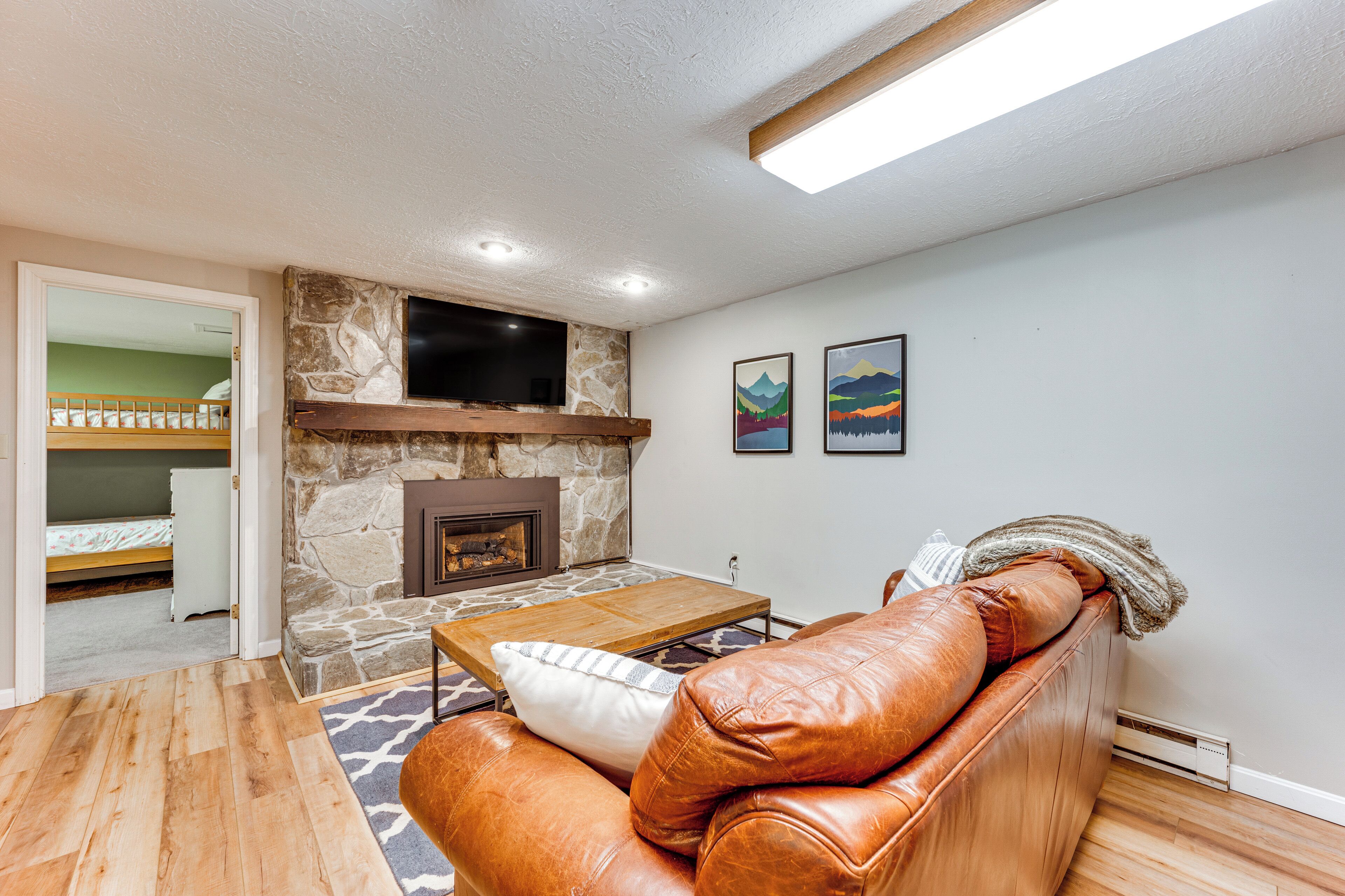 A living room with a stone fireplace, leather sofa, wooden coffee table, and a flat-screen TV mounted above the fireplace.