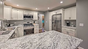 Una cocina moderna con armarios blancos, encimeras de granito, electrodomésticos de acero inoxidable e iluminación empotrada en el techo.