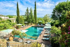 A swimming pool with lounge chairs and umbrellas, surrounded by tall trees and greenery.
