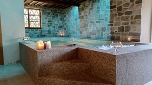 Une pièce aux murs de pierre, avec un jacuzzi carrelé, des bougies et des verres disposés sur une table.