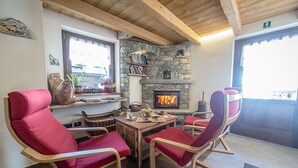 A cozy room with a stone fireplace, wooden ceiling, and red upholstered chairs around a wooden table. - Alpe Rebelle (Bionaz)