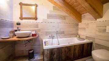 Un baño con tocador de madera, bañera independiente y un inodoro.