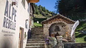 A rustic stone staircase leading to a wooden archway with a sign above. - Alpe Rebelle (Bionaz)