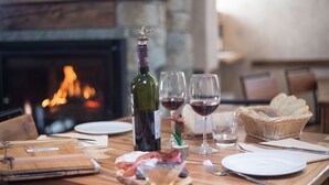A wooden table set for a meal with a bottle of wine, glasses, plates, and a basket of bread. - Alpe Rebelle (Bionaz)