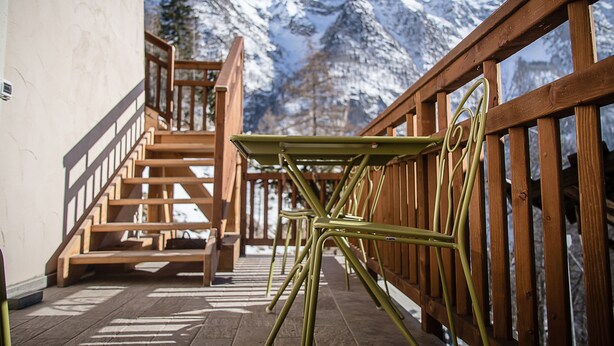 A wooden staircase leading to a balcony with a metal table and chairs, overlooking snow-capped mountains. - Alpe Rebelle (Bionaz)