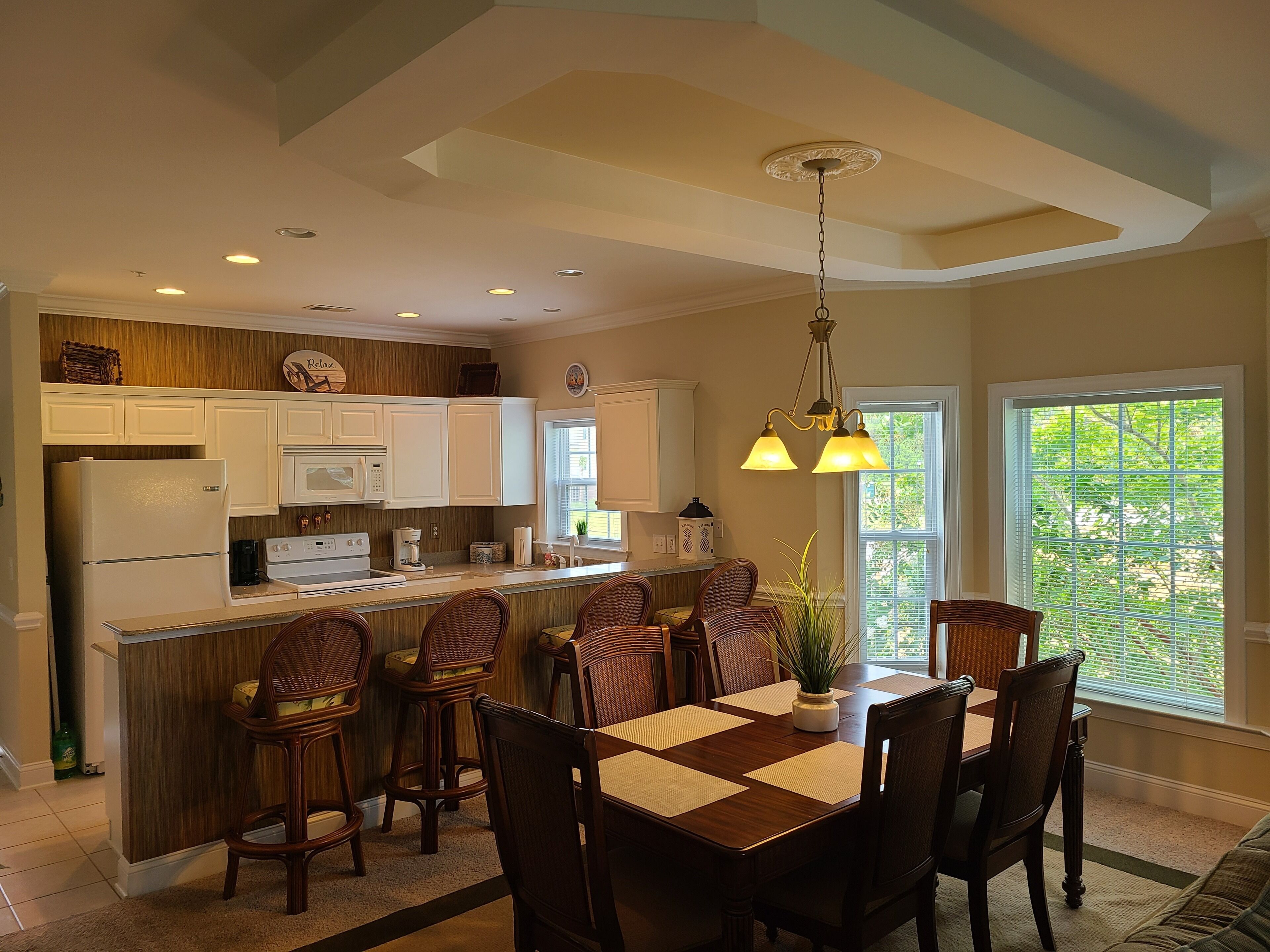 A modern kitchen with white cabinets, a central island with bar stools, and a dining area with a wooden table and chairs.