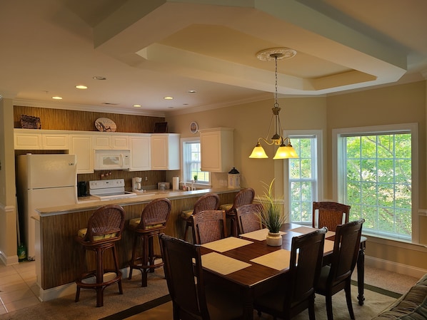 Una cocina moderna con armarios blancos, una isla central con taburetes y un comedor con mesa y sillas de madera.
