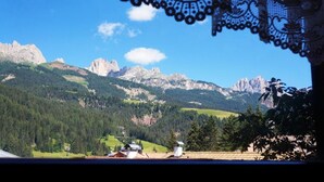 Eine gebirgige Landschaft mit blauem Himmel, einem leicht sichtbaren Spitzenvorhang im Vordergrund und einigen Gebäuden in der Ferne.