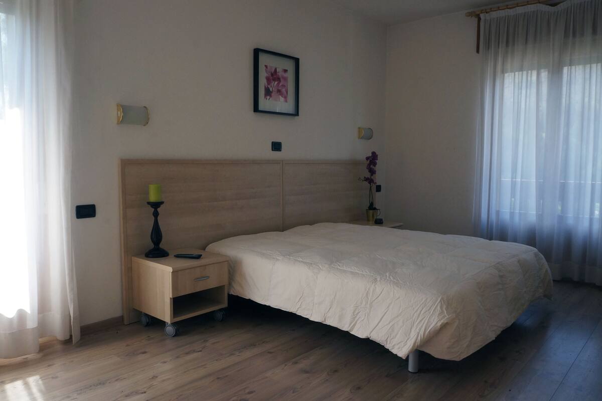 A bedroom with a large bed, a nightstand, a wall-mounted lamp, and a framed picture.