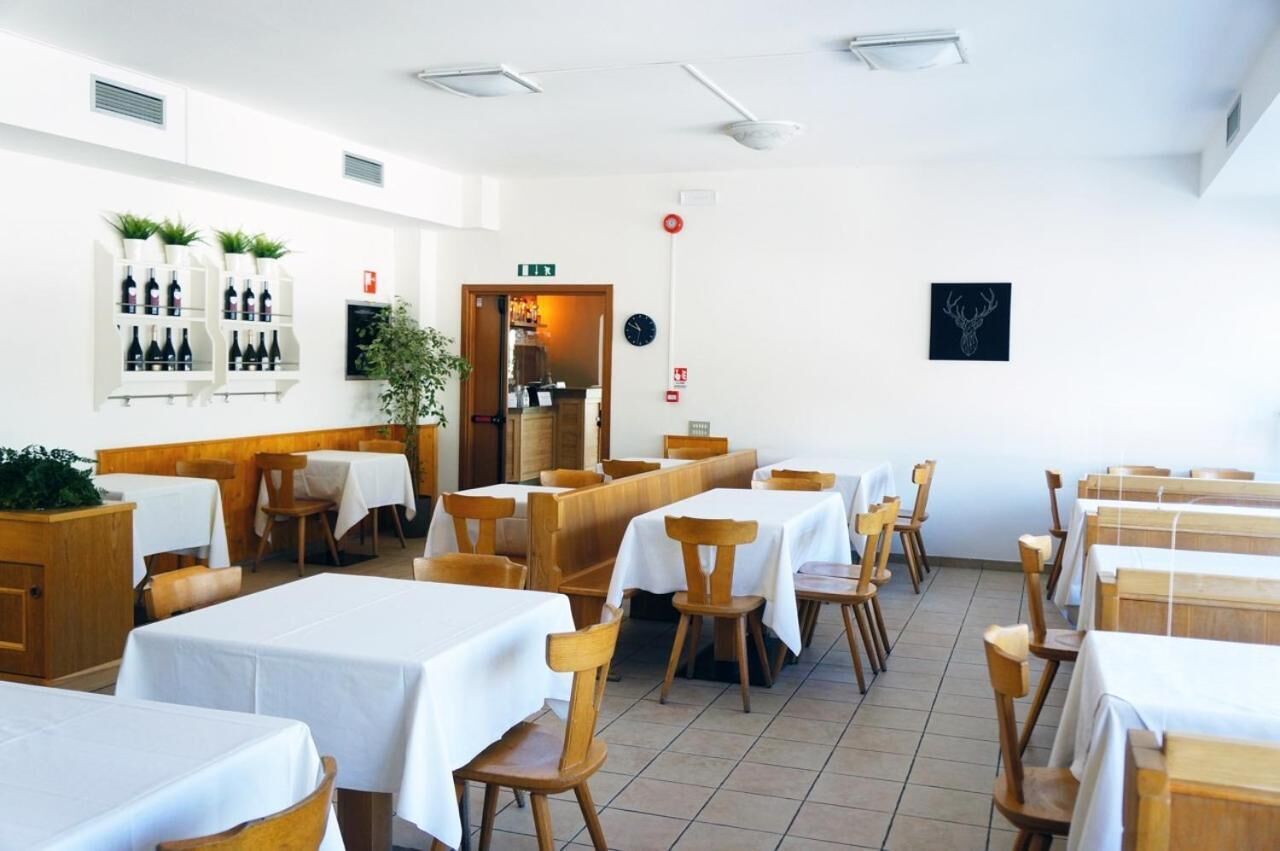 Un ristorante con tavoli e sedie in legno, tovaglie bianche e una dispensa a parete per il vino.