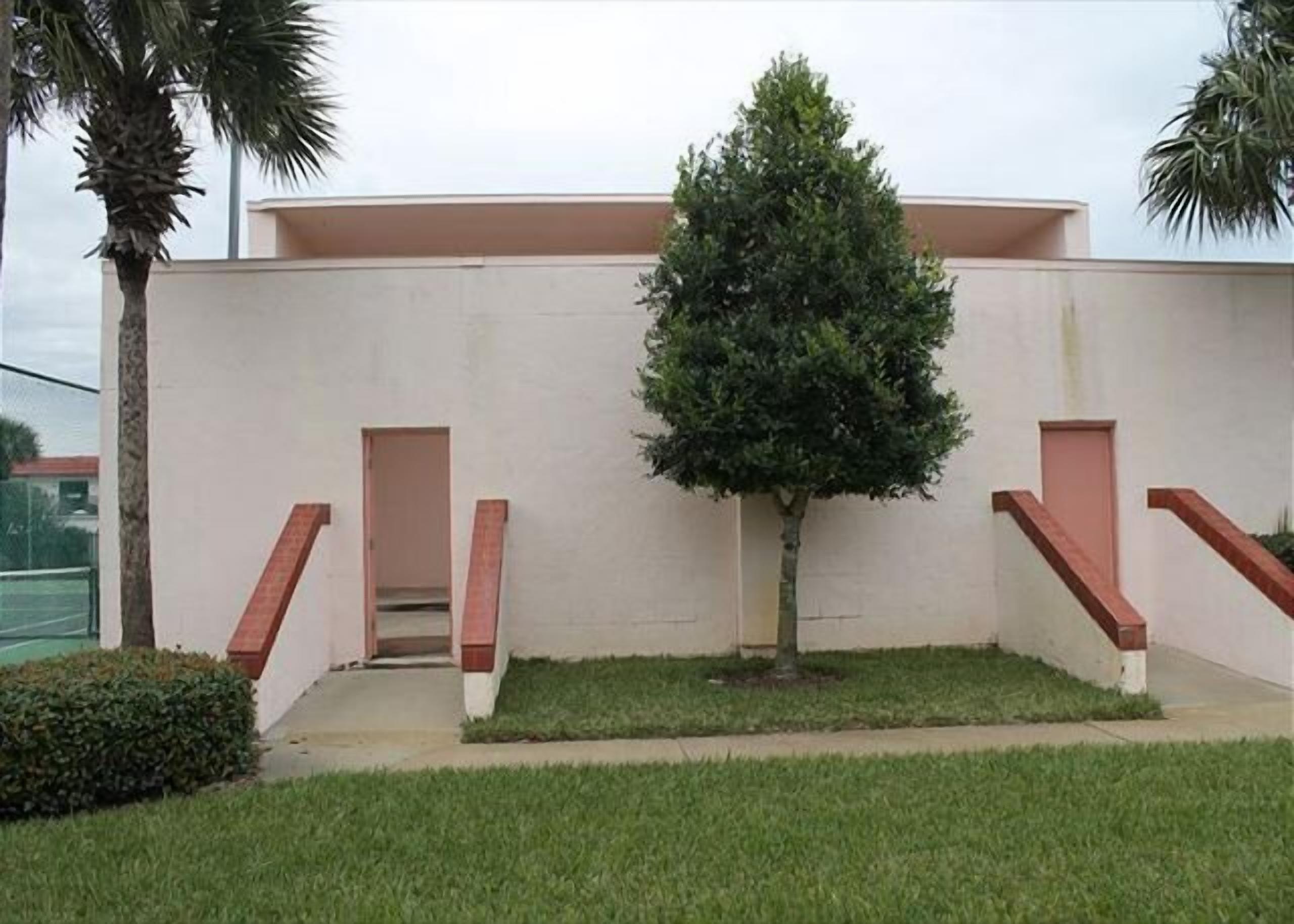 A building with a flat roof, a small tree in the center, and a paved area with stairs leading to an entrance.