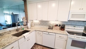 A kitchen with white cabinets, a granite countertop, a dishwasher, a stove, and a toaster. - Sea Place 13239 (St. Augustine)