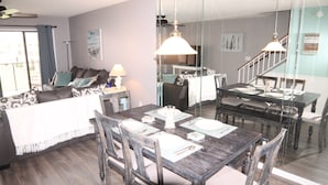 A dining area with a wooden table set for four, surrounded by chairs. A large mirror reflects the room, and a staircase is visible in the background. - Sea Place 13239 (St. Augustine)