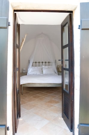 A bedroom with a bed under a canopy, a nightstand, and a tiled floor.