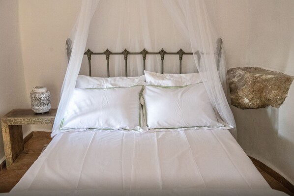 A bed with a canopy, a bedside table, and a decorative stone on the wall. - PositiveSpace Olive Tree - A unique tower-house experience (Lefktro)