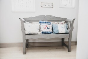 A grey wooden bench with a simple backrest and a flat seat, placed against a white wall.