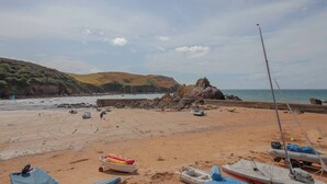 Ein sandiger Strand mit Booten und einer felsigen Landzunge im Hintergrund.