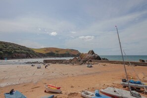 A sandy beach with boats and a rocky outcrop in the background.