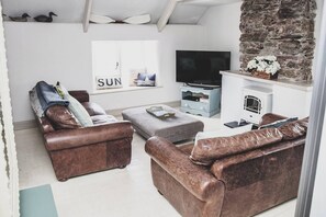 A living room with leather sofas, a television, a fireplace, and a stone wall.