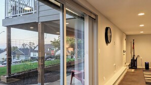 Ein modernes Interieur mit Glastür, die auf einen Balkon führt, einer Wanduhr und einem Staubsauger in der Ecke.