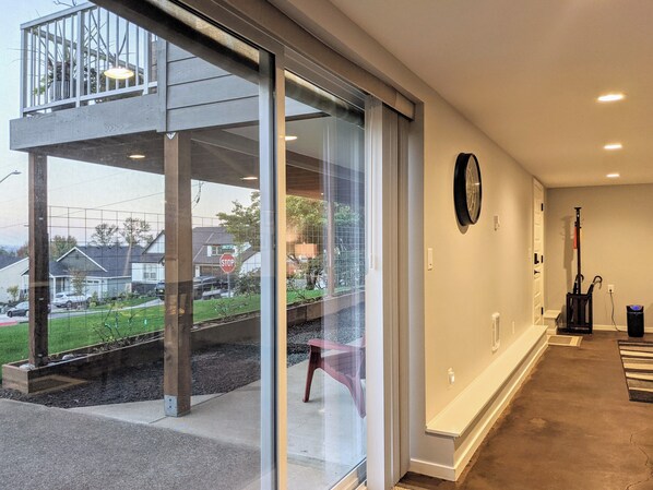 Een modern interieur met een glazen deur naar een balkon, een klok aan de muur en een stofzuiger in de hoek.