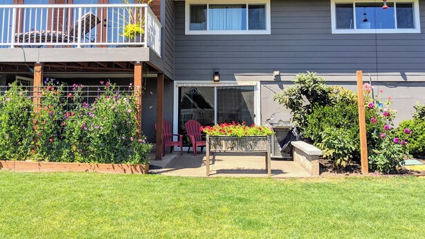 Ein zweistöckiges Haus mit Balkon, einer Terrasse mit Stühlen und einem Garten mit verschiedenen Pflanzen und Blumen.