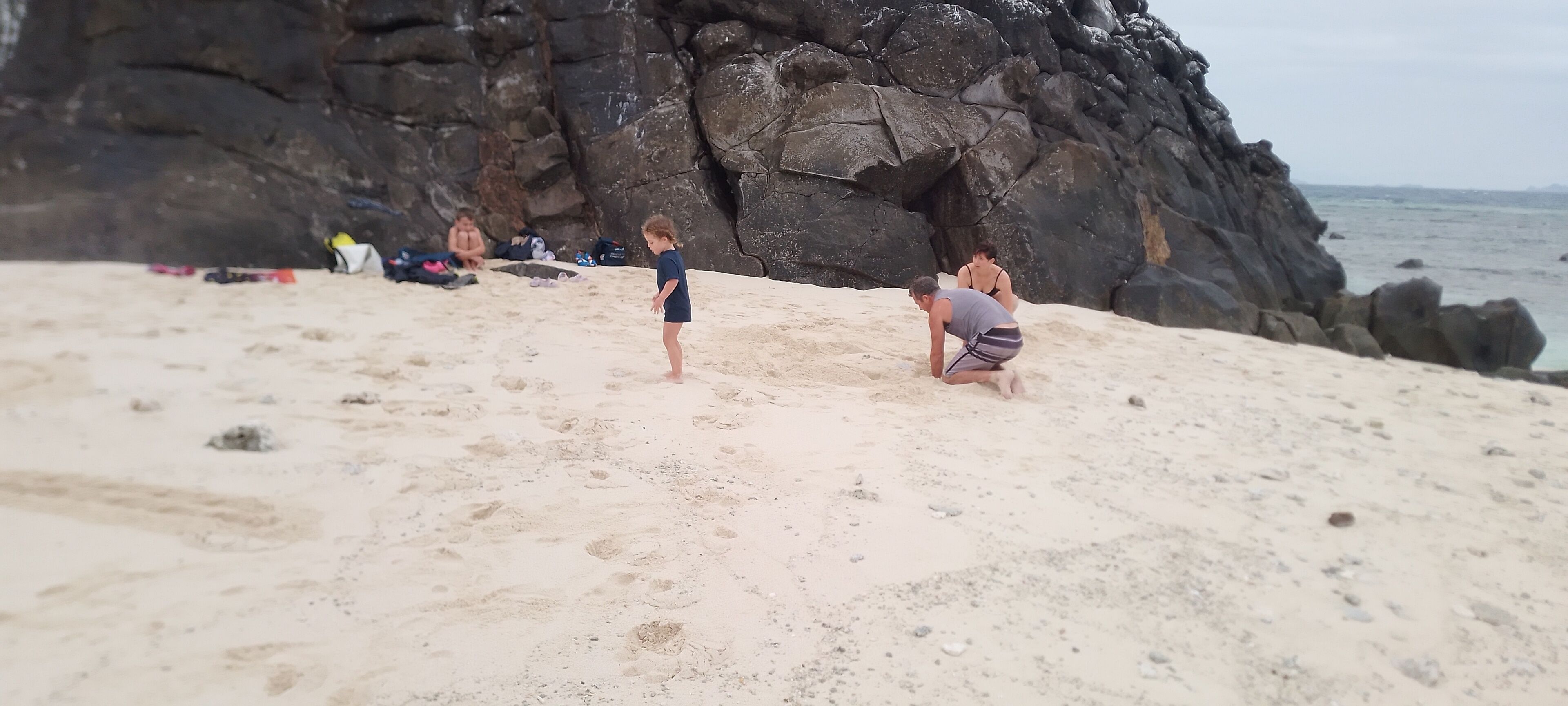 Una playa arenosa con formaciones rocosas al fondo.