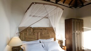 Un lit avec une tête de lit en bois, une literie blanche et un baldaquin. Il y a deux tables de chevet avec des lampes. On peut apercevoir une armoire en bois dans un coin de la pièce.