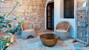 Une cour accueillante, avec des murs en pierre, deux fauteuils en osier, un grand saladier en fibres tressées et une porte décorative.